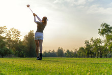 Sport Healthy. Asian Sporty Woman Golf Player Doing Golf Swing Tee Off On The Green Sunset Evening Time, She Presumably Does Exercise. Healthy And Lifestyle Concept.