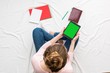 © Анастасия Семашко - Woman holding a tablet, sitting on a white crumpled blanket, red notebook, women's feet. Women's hands. Background with copy space, for advertisement. Top view