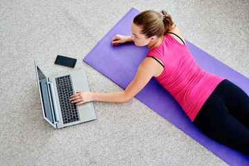 Beautiful young woman doing working out exercise on floor at home and using laptop, online training, copy space. Yoga, pilates exercising. Sport, healthy lifestyle concept