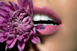 © Andreas Kuehn - Close up of woman's lips with purple flower between her teeth