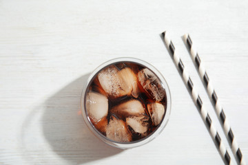 Wall Mural - Glass of refreshing cola with ice cubes on white wooden background, top view