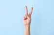 Woman showing V letter on color background, closeup. Sign language