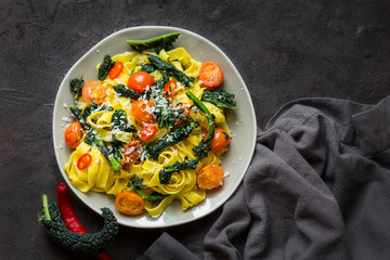 Poster - Tagliatelle pasta with kale, tomatoes, pepper and parmesan cheese. Dark background.