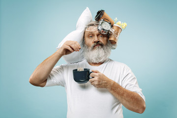 Surprised senior man drinking tea after sleeping at home or office having too much work. Bored businessman with pillow and hourglass. The busy, boring, worried, be late, concerned, sleep day