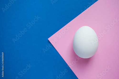 A White Single Egg On Dark Blue And Pastel Pink Background With