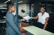 © JonoErasmus - Attractive black receptionist handing over paperwork to businesswoman