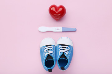 Pregnancy test with baby boots and red heart on pink background