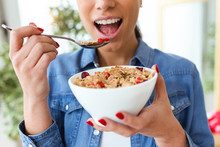 Smiling Young Woman Eating Breakfast Cereals Of Bowl At Home.