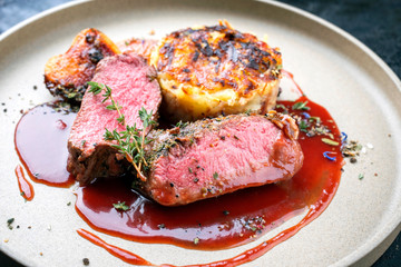 Traditional saddle of venison with Swiss rösti, quince and orange slices in game red wine sauce as closeup on a modern design plate