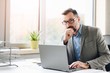 © Daniel Jędzura - Thoughtful middle aged handsome businessman in shirt working on laptop computer in office
