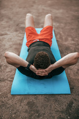 Wall Mural - Male athlete, in the summer in city, lying on the athletic mat trains your abdominal muscles. Resting after a workout in the fresh air, in casual clothes and red shorts. Shakes the press.