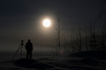 Wall Mural - photographer standing in snow photographing winter landscape. full moon and stars on night sky.