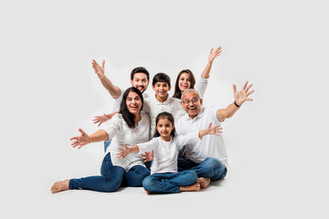 Wall Mural - indian/asian family sitting over white background. senior and young couple with kids wearing white top and blue jeans. selective focus