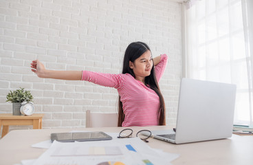 Poster - Asian woman stretching arm up when working on laptop at white brick wall in home.Work at home concept.relax after hard work.