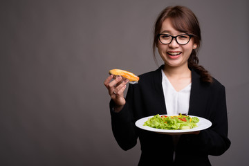 Happy Asian businesswoman holding hot dog and salad