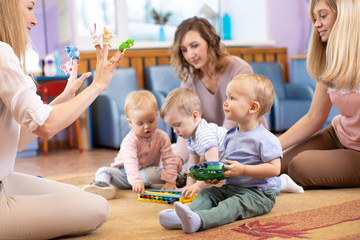  Young moms and their kids together in club. Babies play with musical toys
