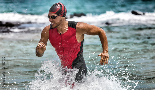 Fototapeta na szkło Triathlon pływanie człowiek zaczyna brakować wody podczas wyścigu ironman. Męski triathlon kończący zawody w czasie pływania. Dopasuj pływaka sportowca do biegania wyznaczonego z wody w profesjonalnym tri-suitu.