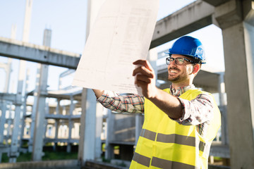 Portrait of male site contractor engineer with hard hat holding blue print paper