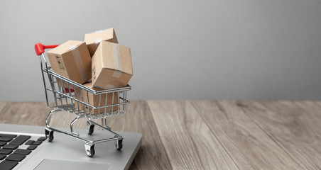 Delivery of the order from the online store. Online shopping. Boxes with goods in the shopping basket on the table with laptop. Copy space for text.