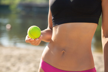 Closeup shot of sporty model with perfect body holding tennis ball. Copy space