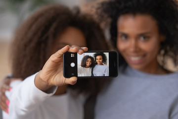 Sticker - Happy African American teen girl holding smartphone, making selfie with young mom or nanny, smiling black mother and teenage daughter have fun together, posing for self-portrait picture at home