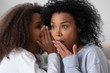 African American teenage girl tell secret to surprised young mom or nanny, teen daughter share gossip whispering in ear to shocked black mother, young parent and kid spend time together talking