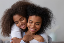 Sweet Teenage Daughter Hug Young African American Mom From Behind Showing Love And Care, Tender Teen Girl Embrace Mother Or Nanny, Parent And Child Have Close Intimate Moment Together