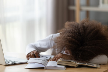 Wall Mural - Tired little African American girl fall asleep at table studying with textbooks and laptop, exhausted teenager sleep when preparing homework with handbooks, bored pupil nap doing housework