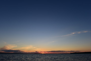 Wall Mural - Sunset is a small bright point on the horizon the sun is infinite in space the blue of the sky and the water of the lake