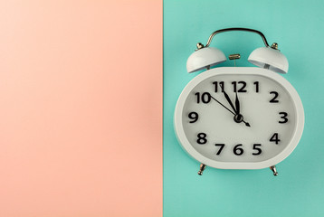 white vintage alarm clock on pink and blue background. - top view.