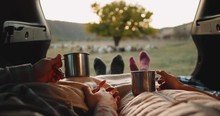 Trip on countryside for a couple who are lying down on the car trunk and wearing a cozy socks with a blanket over and holding a iron cups with tea spending a nice time. 4k