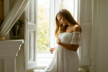 Wall Mural - Young pregnant woman standing by the window