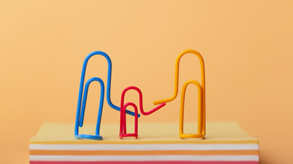 three clips: mom, dad and child on a colored background holding hands sitting on a stack of tear-off leaves, a creative idea of the concept of a happy family life