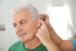 Young man putting hearing aid in father's ear indoors