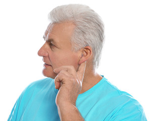 Wall Mural - Mature man adjusting hearing aid on white background