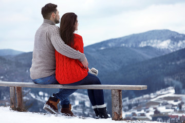 Poster - Couple sitting on bench and enjoying mountain landscape, space for text. Winter vacation