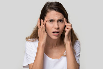 Stressed young woman confused about facial wrinkles aging skin on forehead or crows feet looking at camera isolated on studio background, upset worried girl having headache touching temples, portrait