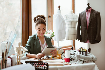 design studio. young woman tailor with digital tablet is modeling new clothes