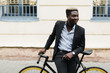 © F8  \ Suport Ukraine - Handsome young Afro American man in casual clothes is looking away while leaning on his bike in the street