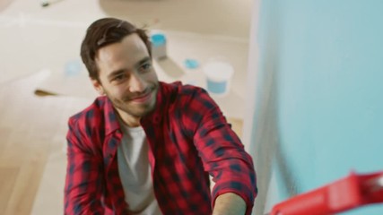 Wall Mural - Close Up Shot of a Man in Brown Jeans and Red Checked Shirt Painting a Wall with a Roller. Paint Color is Light Blue. Room Renovations at Home. Shot From Above.