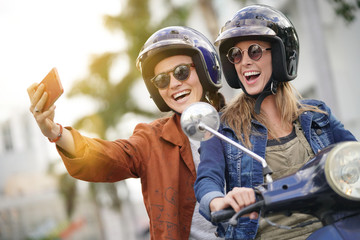 Happy young women taking a selfie on scooter in city