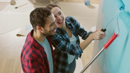 Wall Mural - Young Beautiful Couple Decorate Their New Apartment. Husband and Wife are Painting the Wall with Rollers that are Dipped in Light Blue Paint. They Hug and Kiss. Renovations at Home.