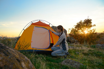 Wall Mural - young woman assembling the tent at sunset in the mountains. adventure and travel.