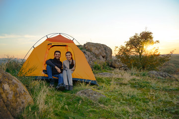 Wall Mural - young couple sitting near tent at beautirul evening in the mountains. adventure and family travel.
