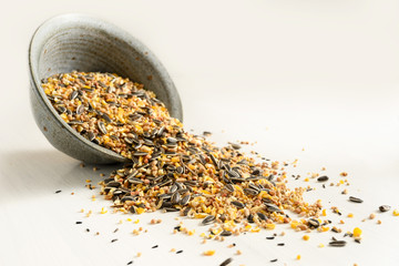 bird food from mixed seeds like sunflower, corn, millet and more, are falling out of a bowl on a light background, copy space