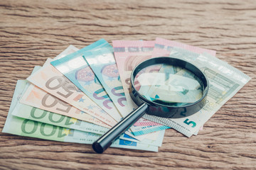 Wall Mural - Finance saving, tax, investment or searching for yield concept, magnifier glass on pile of Euro banknotes on wooden table, European Union government economics situation