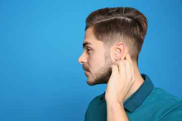 Wall Mural - Young man adjusting hearing aid on color background. Space for text