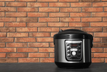 Modern Electric Multi Cooker On Table Near Brick Wall. Space For Text