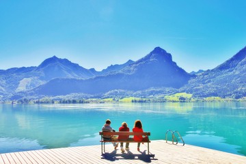 Three mature ladies enjoying a nice day outside. Beautiful view at mountains, senior woman with hat on a wooden jetty at lake. Summer vacation, travel outdoors, nature weekend getaway concept