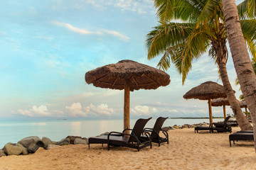 Wall Mural - Zen scene of chaise lounge chairs on beach with thatched umbrellas and calm ocean